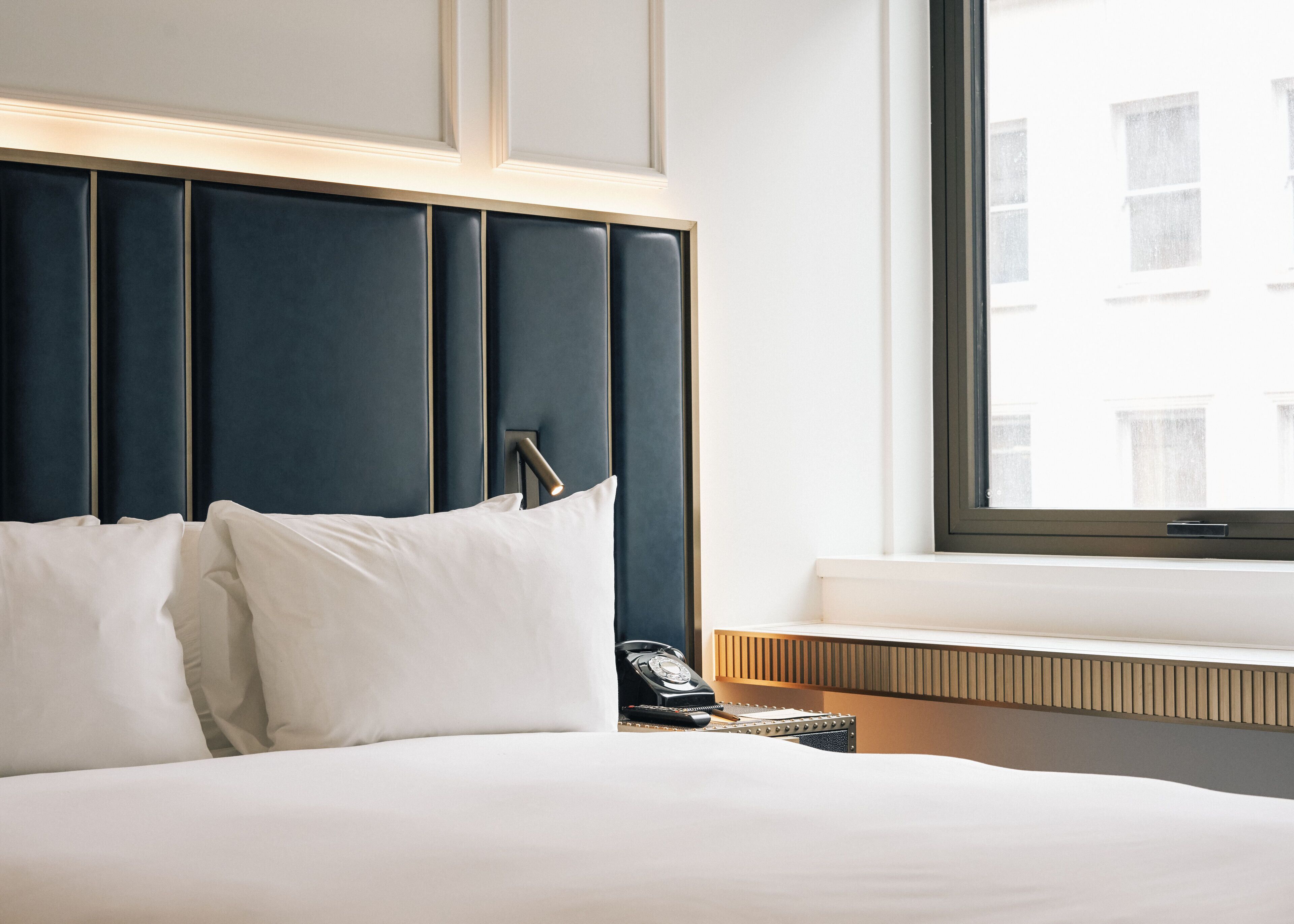 A neatly made bed with white linens, a dark headboard, and a bedside telephone.
