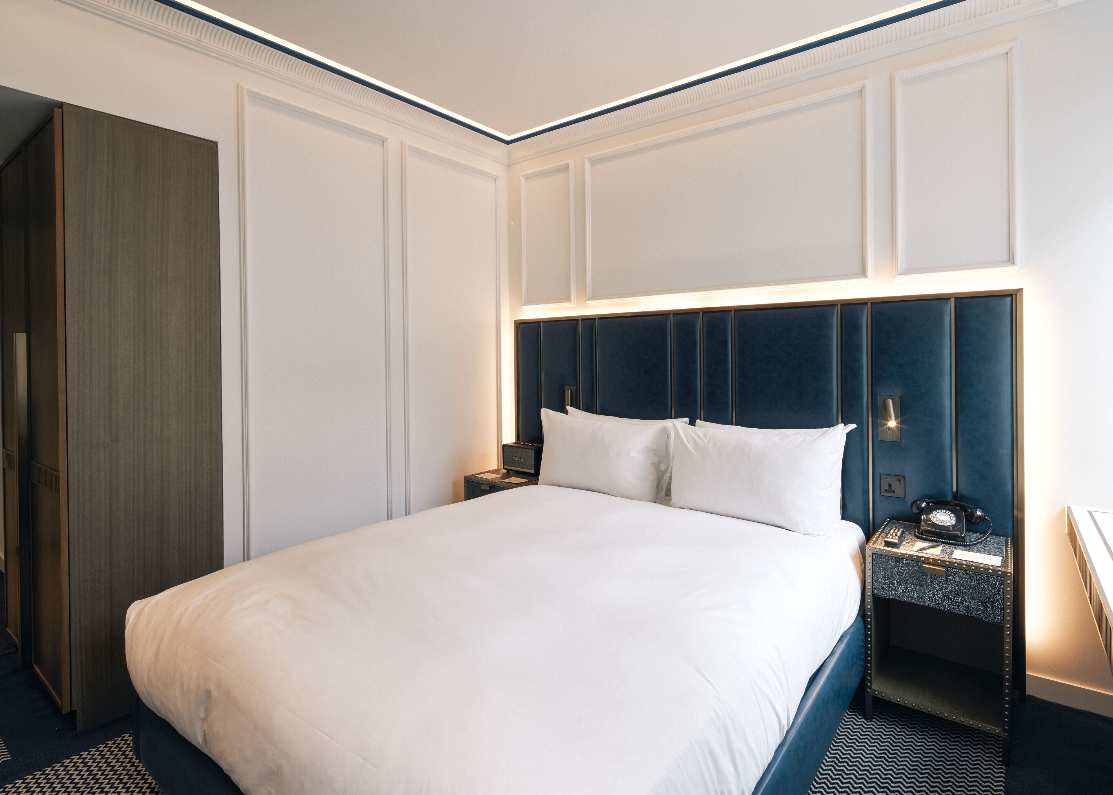 A hotel room with a large bed, a nightstand with a telephone, and a wardrobe.