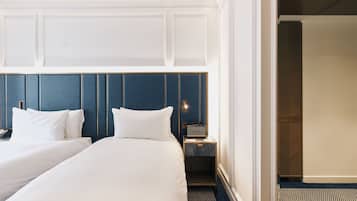 Habitación de hotel con dos camas, una mesita de noche con lámpara y vista al pasillo.