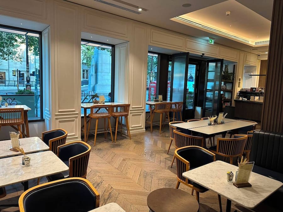 Interior de restaurante con varias mesas y sillas, ventanas amplias y vista a la calle.