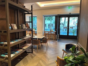 Une bibliothèque avec des étagères, des tables, des chaises et une grande fenêtre donnant sur la rue.