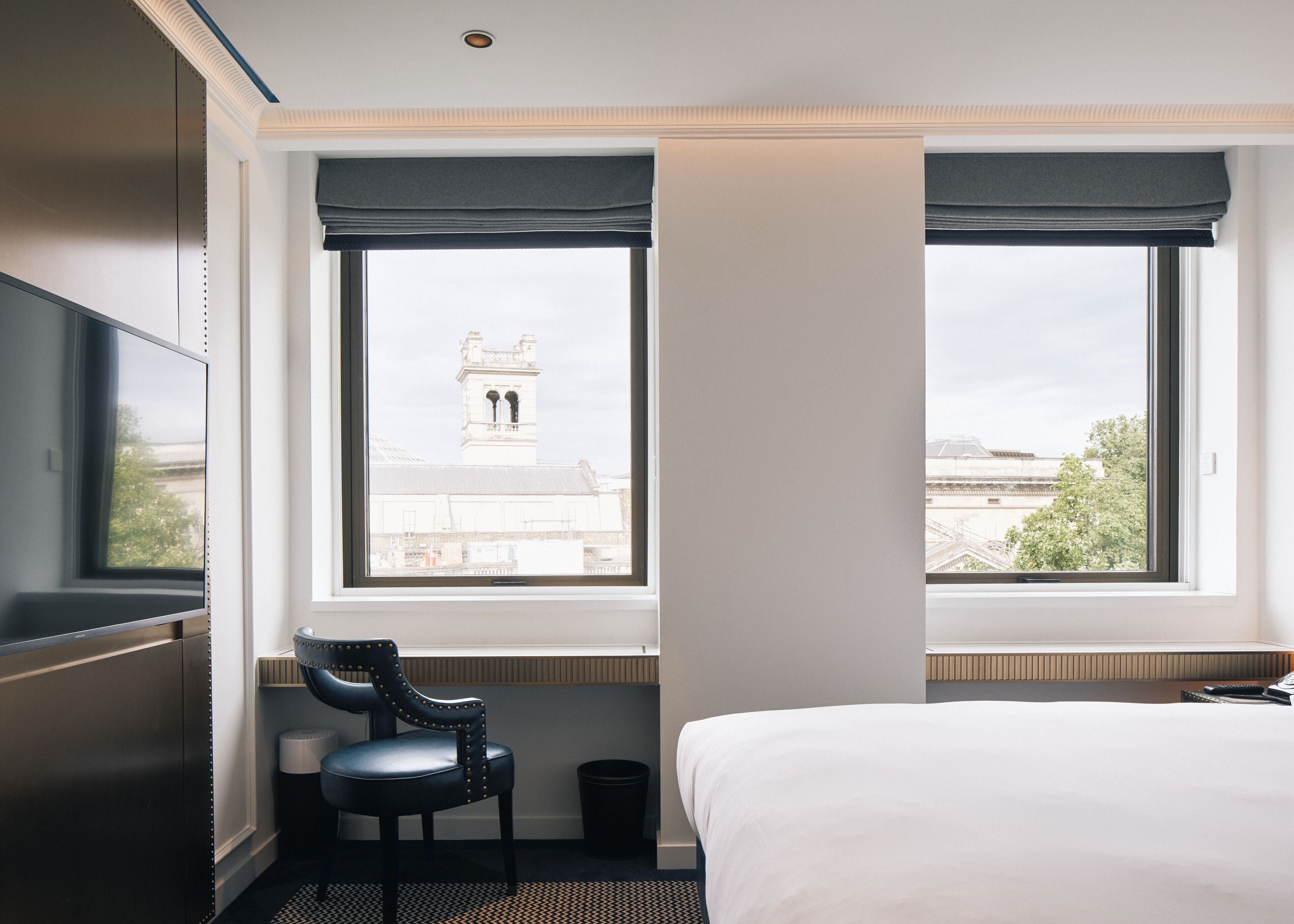 A hotel room with a bed, a chair, a TV, and a window with a view of a building.