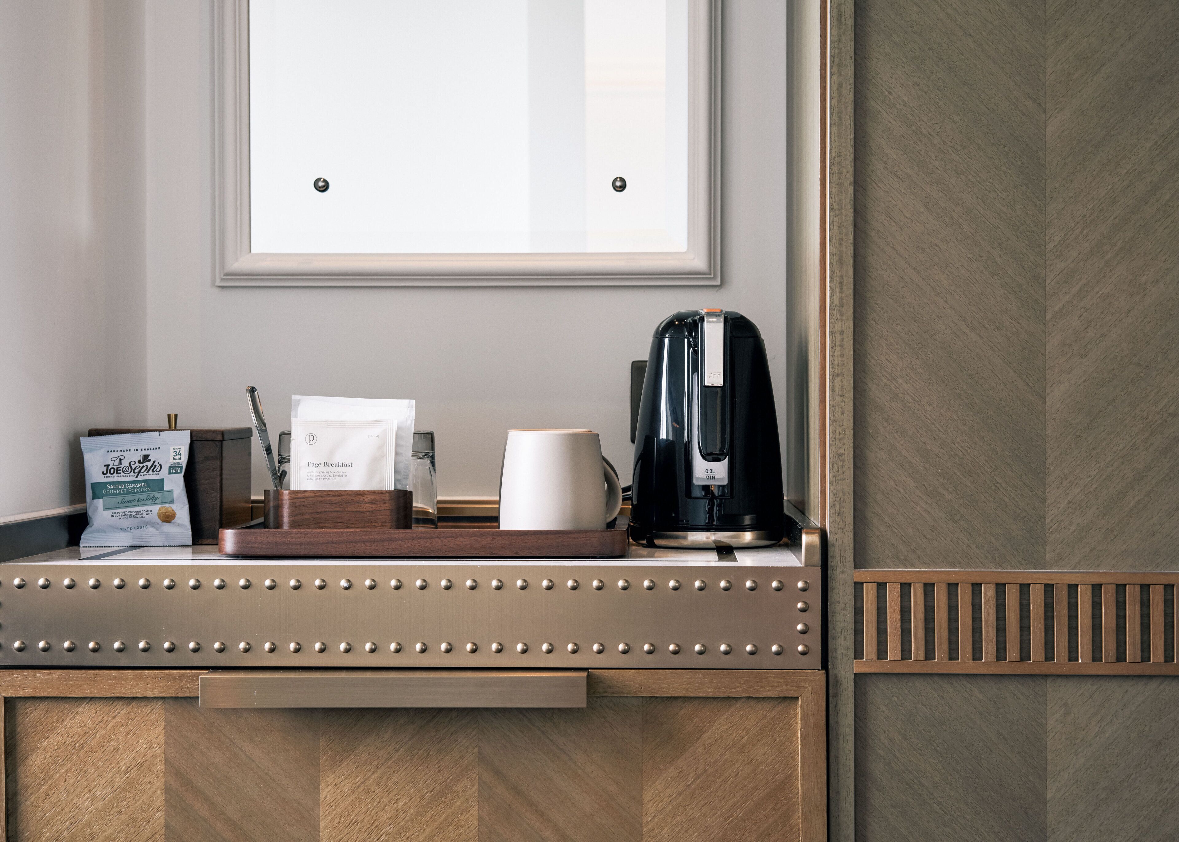 Mostrador de hotel con cafetera, taza, paquete de café y un cuadro en la pared.