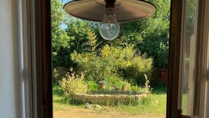 A view through a glass door into a garden with a hanging light fixture. - Alfred and George, Le Gîte (Sainpuits)