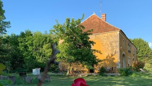 A rustic building with a tiled roof, surrounded by a grassy area and trees. - Alfred and George, Le Gîte (Sainpuits)