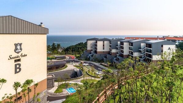A modern building with a sign reading "Seaside Arden B" and a view of a coastal area with a road and greenery. - Seaside Arden (Seogwipo)