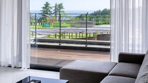 A modern living room with a large window overlooking a garden and a train track. - Seaside Arden (Seogwipo)