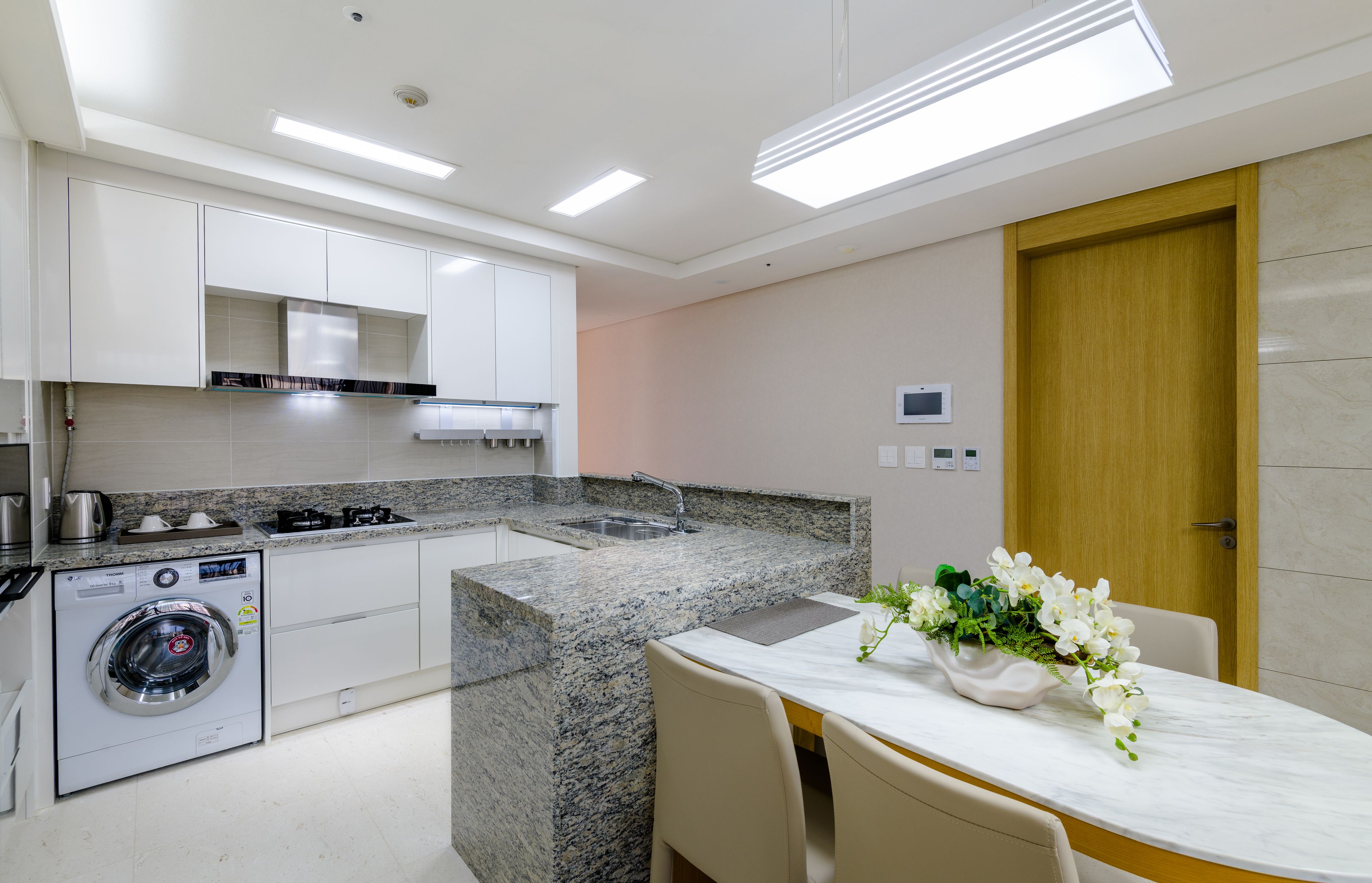A modern kitchen with built-in appliances, a granite countertop, and a dining area with a marble table and chairs.