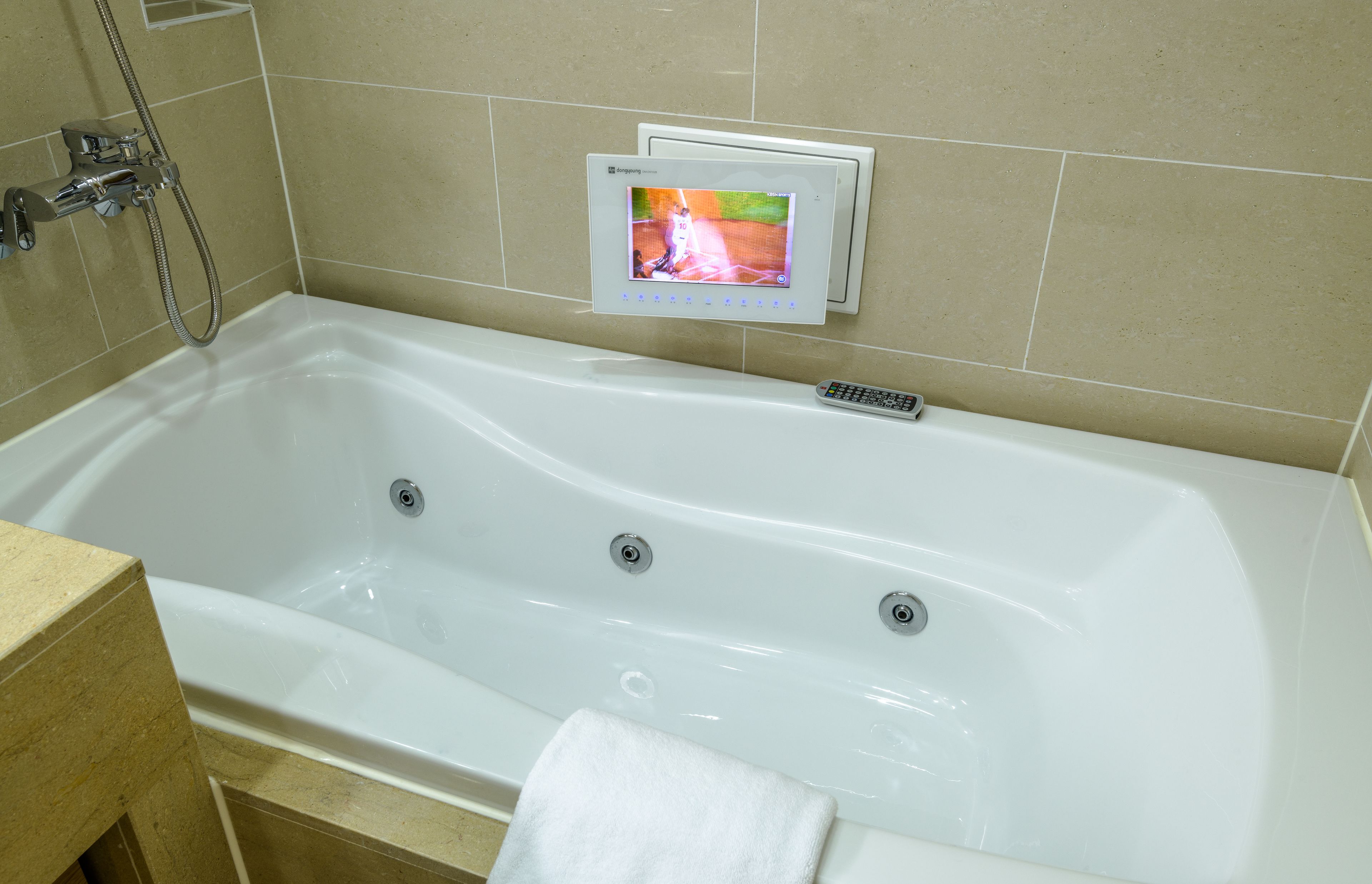 A modern bathroom with a white bathtub, a handheld showerhead, and a built-in television screen.