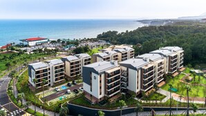 A modern hotel complex with multiple buildings, a parking area, and a view of the ocean. - Seaside Arden (Seogwipo)