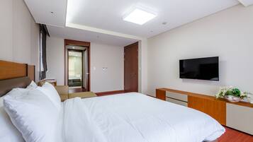 Habitación de hotel con una cama grande, un televisor de pantalla plana montado en la pared, un cabecero de madera, una mesita de noche y una pequeña planta en el tocador.