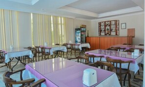 A dining area with tables and chairs, a water dispenser, and a refrigerator. - Efsanem Hotel (Ayvalik)