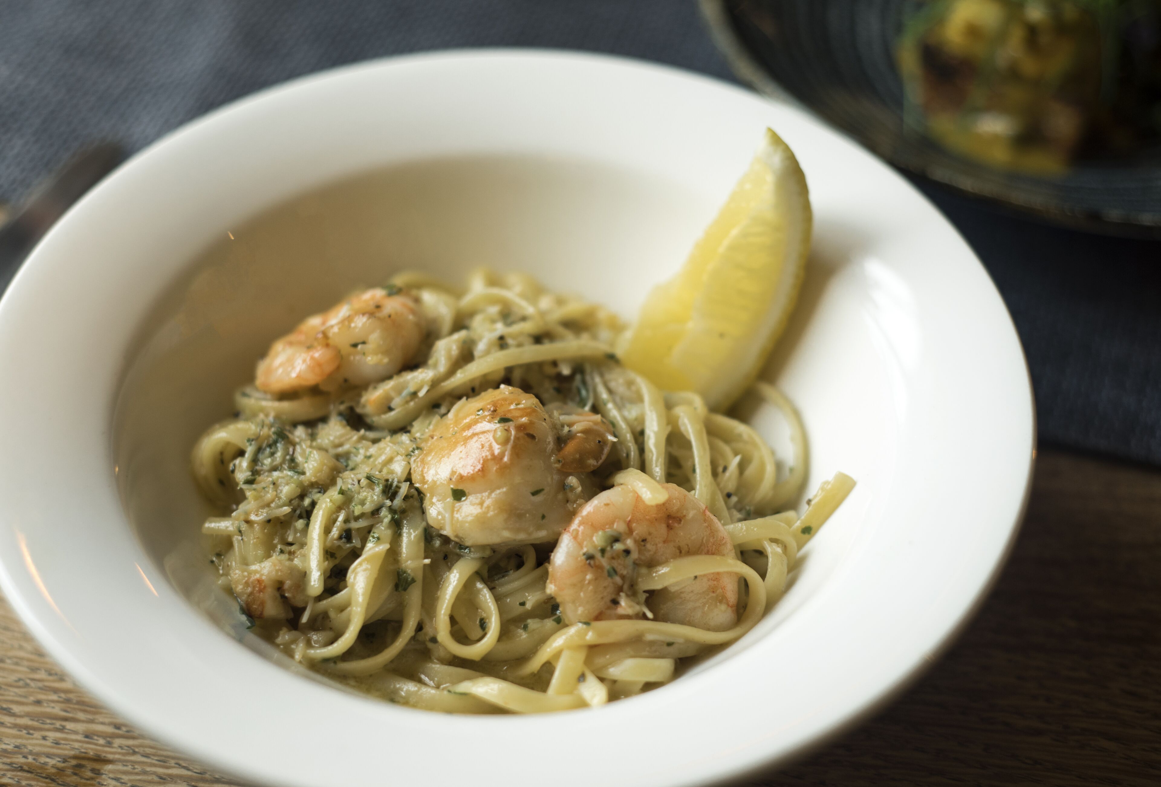 A bowl of pasta with shrimp and a lemon wedge.