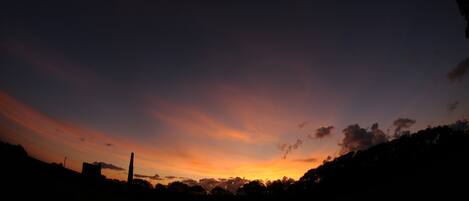 A sunset over a landscape with silhouettes of buildings and trees.