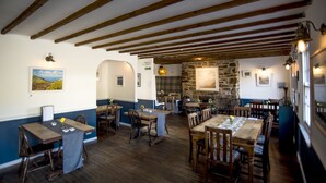 A restaurant with wooden tables and chairs, stone walls, and a view of the countryside. - Victoria Inn (Penzance)