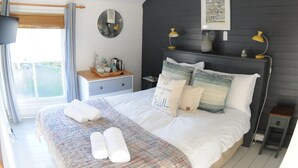 A bedroom with a large bed, bedside tables, a ceiling light, a window with curtains, and a wall-mounted clock. - Victoria Inn (Penzance)
