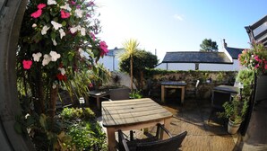 An outdoor patio area with a wooden table and chairs, surrounded by potted plants and flowers. - Victoria Inn (Penzance)