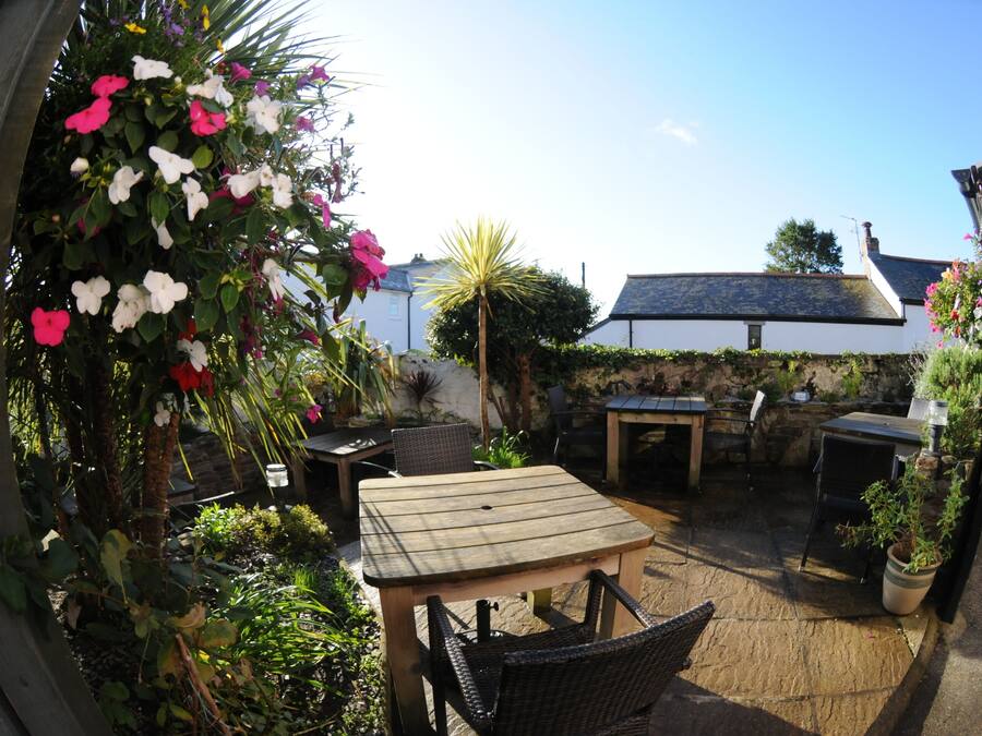 Ein Terrassenbereich im Freien mit einem Holztisch und Stühlen, umgeben von Blumentöpfen und Blumen.