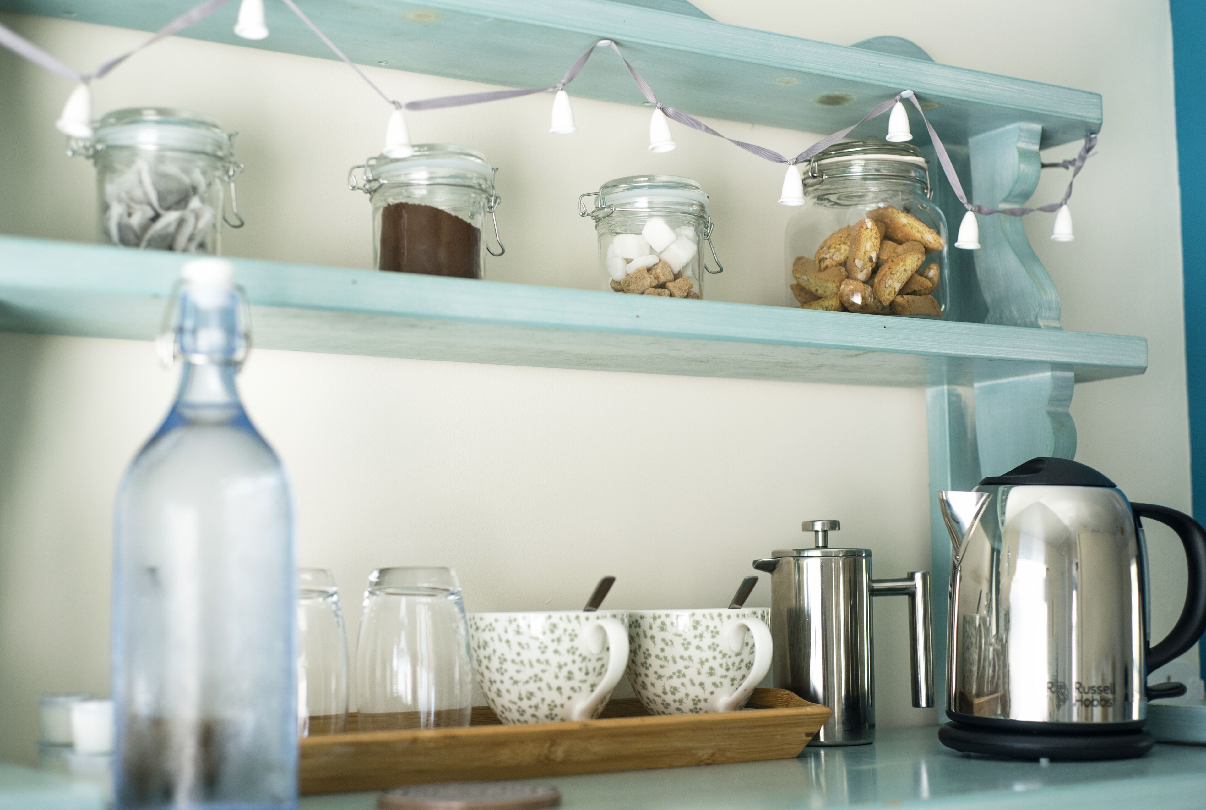 A kitchen counter with a coffee maker, teapot, and jars on a shelf.