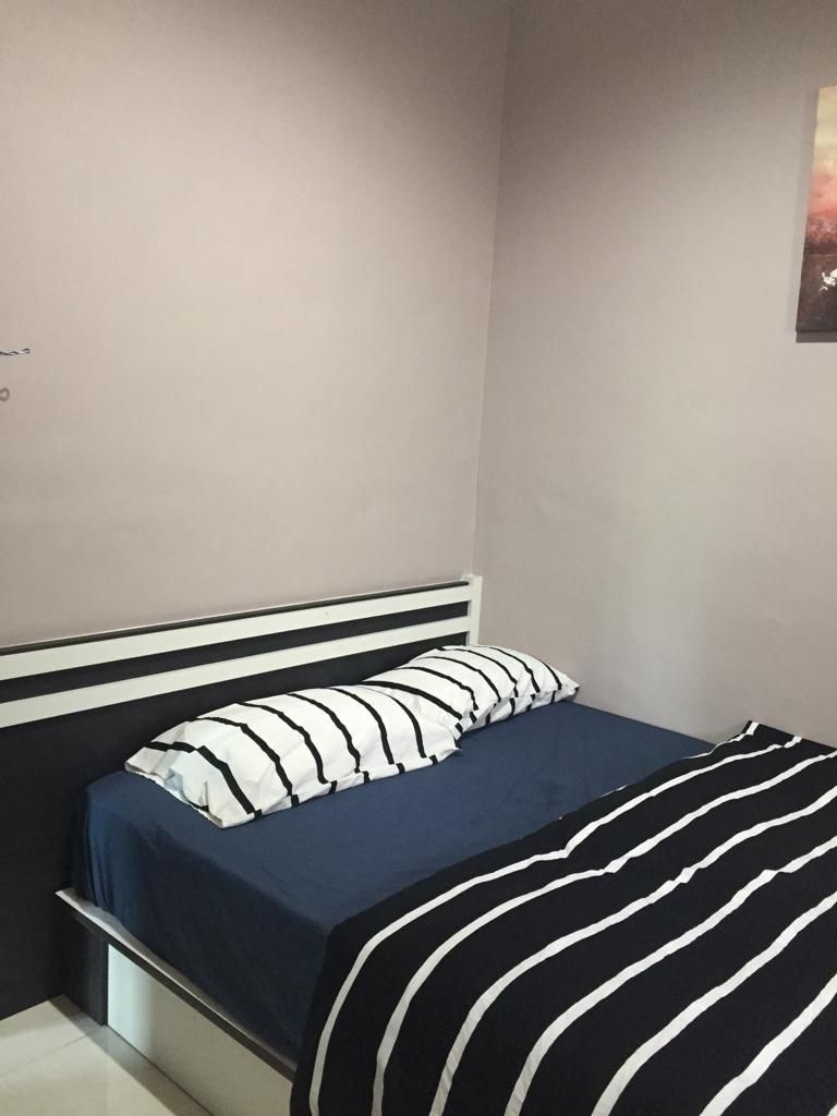A bed with a striped pillow and a striped blanket, a white headboard, and a plain wall.