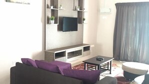 Ein Wohnzimmer mit einem dunklen Sofa, einem Flachbildfernseher und einem Deckenventilator.