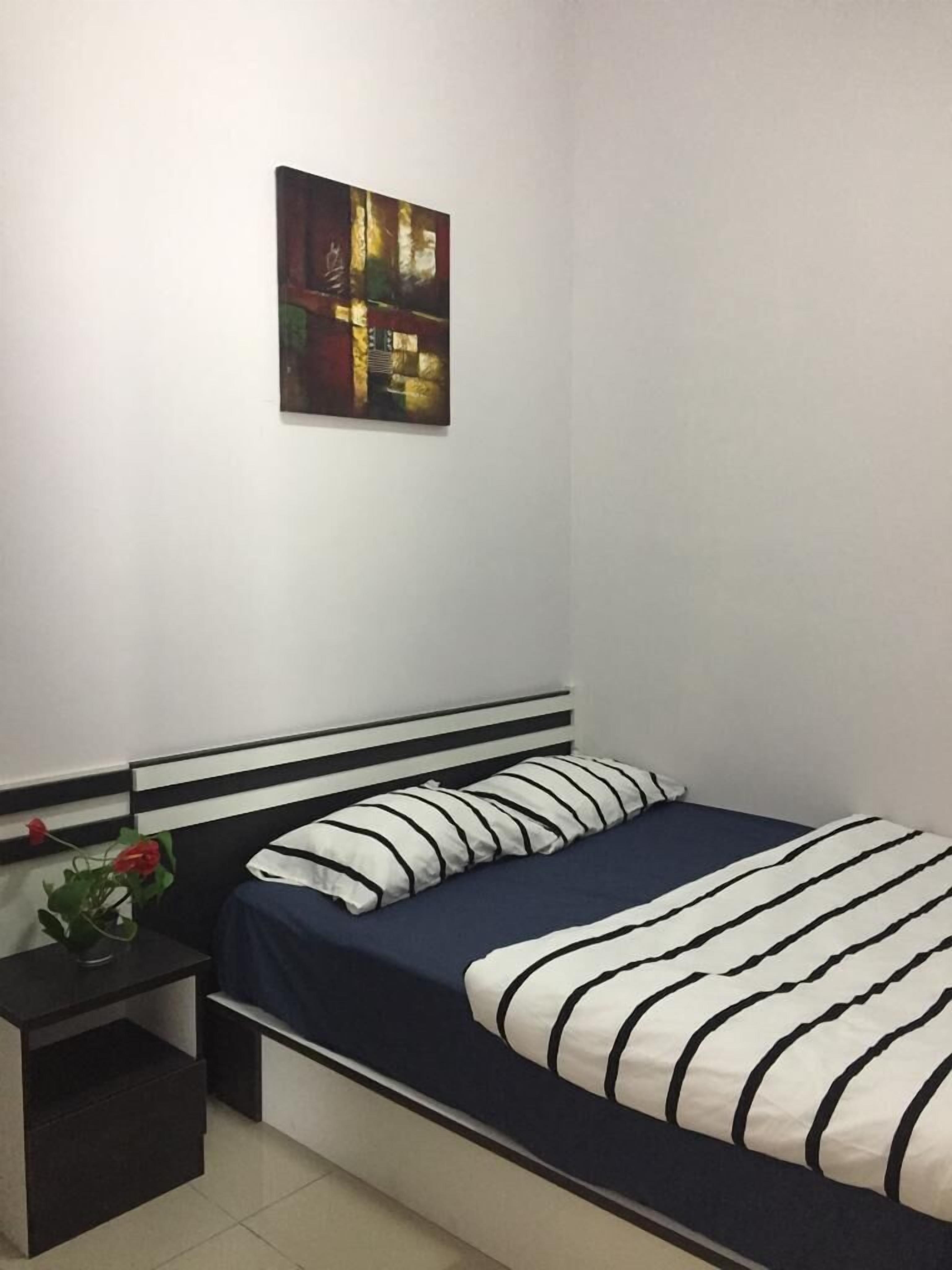 A single bed with a striped bedspread, a bedside table with a plant, and a painting on the wall.