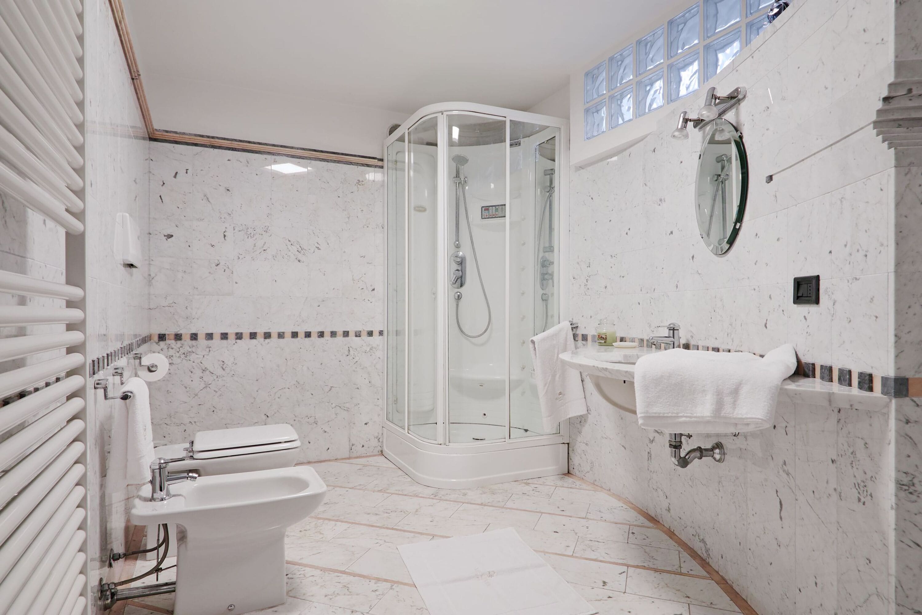 A modern bathroom with a glass-enclosed shower, a bidet, a sink with a towel, and a mirror on the wall.