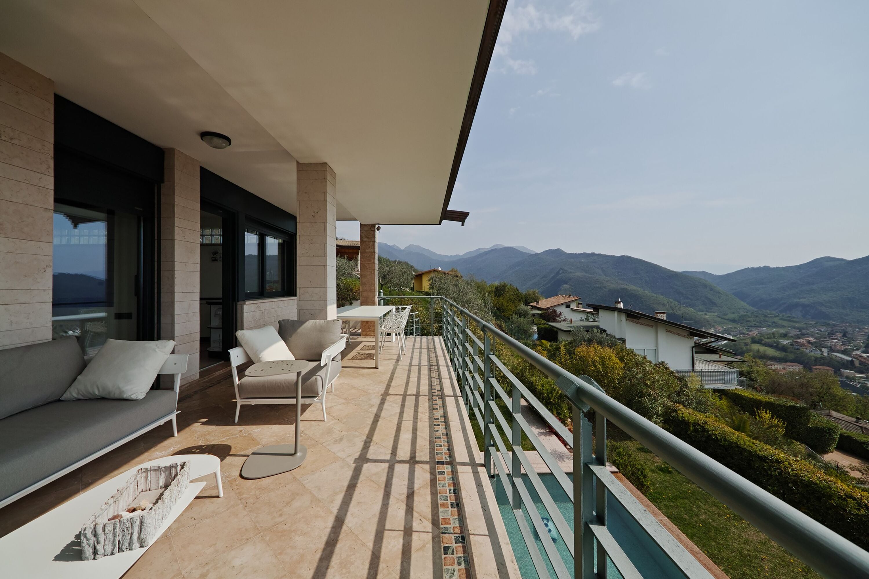 A balcony with a view of mountains, a sofa, and a dining area with chairs.