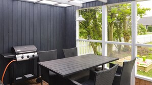 Eine überdachte Terrasse im Freien mit Grill, Tisch und Stühlen.