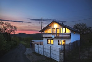 Una casa de dos pisos con un balcón, cerca viva de madera y un letrero que indica que es una casa de huéspedes.