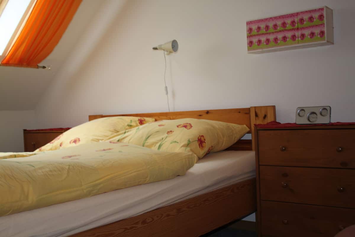 Ein Schlafzimmer mit einem hölzernen Bett, einem Nachttisch mit Radio und einem Wandheizkörper.