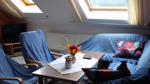 A room with a sofa, a table with a vase of flowers, and a television. - Ferienwohnungen Hees (Emmerzhausen)