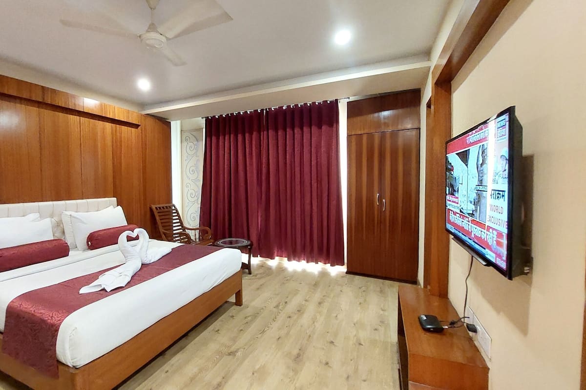 A hotel room with a large bed, wooden paneling, a television, and a wardrobe.