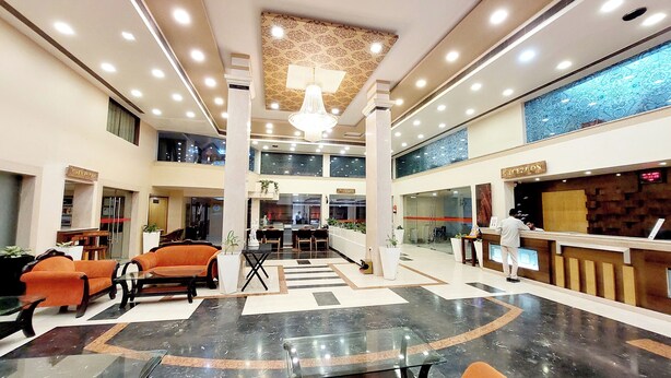 Un'hall d'albergo con reception, area salotto con sedie, un lampadario e un soffitto decorato.