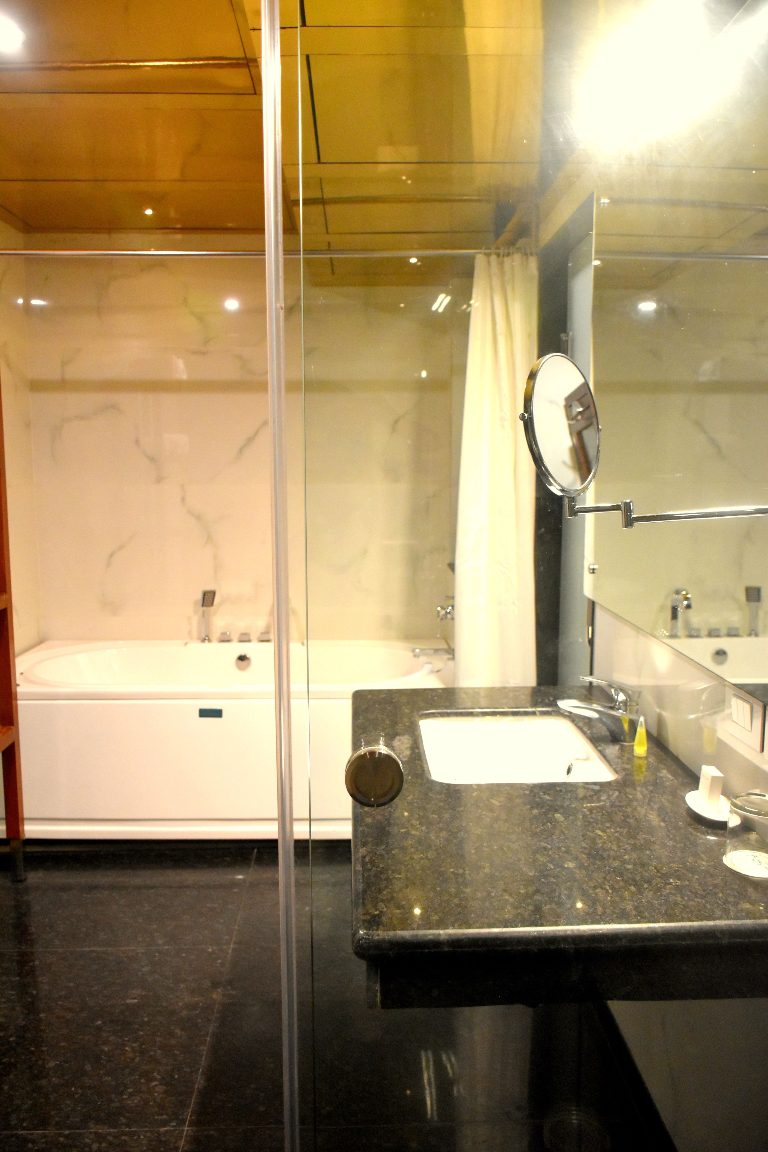 A modern bathroom with a glass shower enclosure, a separate bathtub, and a granite countertop with a sink and mirror.