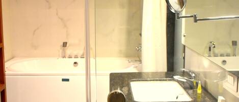 A modern bathroom with a glass shower enclosure, a separate bathtub, and a granite countertop with a sink and mirror.