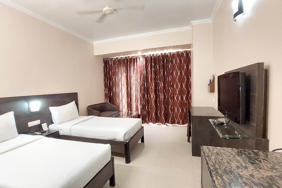 A hotel room with two beds, a desk, a TV, and a ceiling fan.