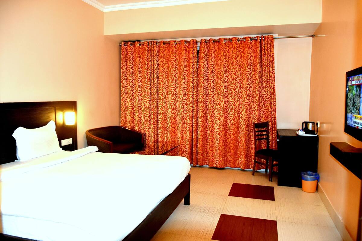 A hotel room with a bed, a desk, a chair, a television, and a curtain.