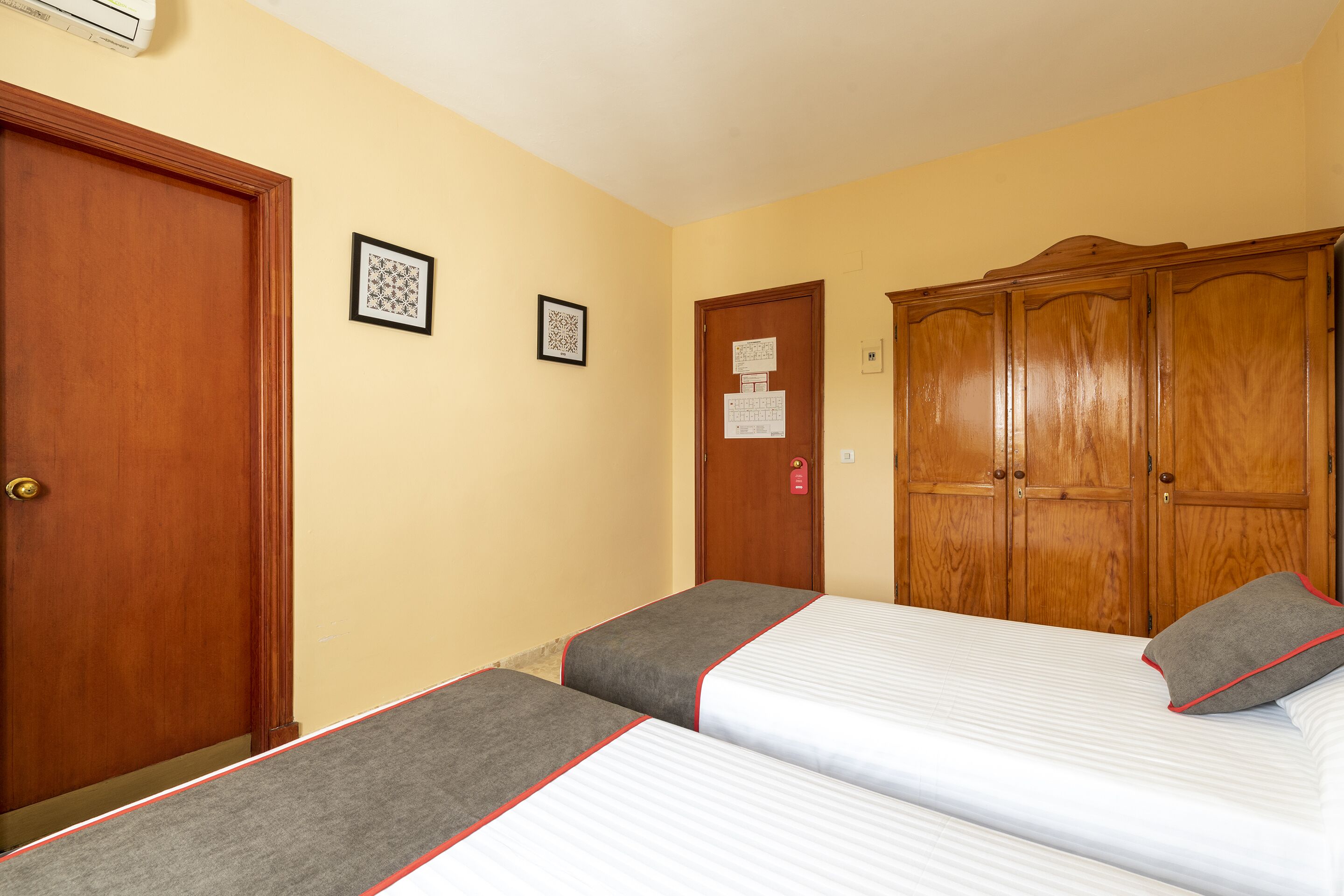 A hotel room with two beds, wooden wardrobe, and two framed pictures on the wall.