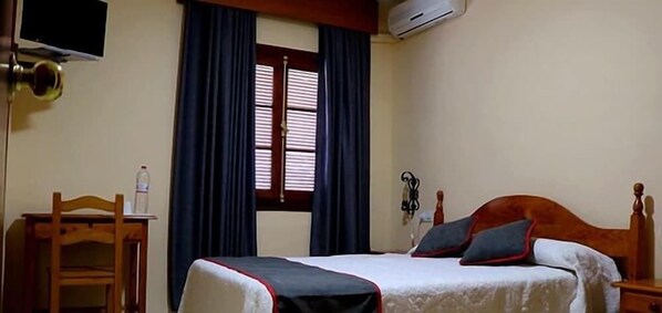 Habitación de hotel con cama, una silla de madera, escritorio, televisor y unidad de aire acondicionado.