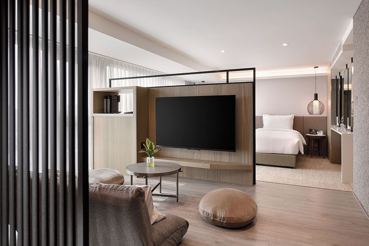 A modern hotel room with a large flat-screen TV, a sofa, a round coffee table, and a bed.