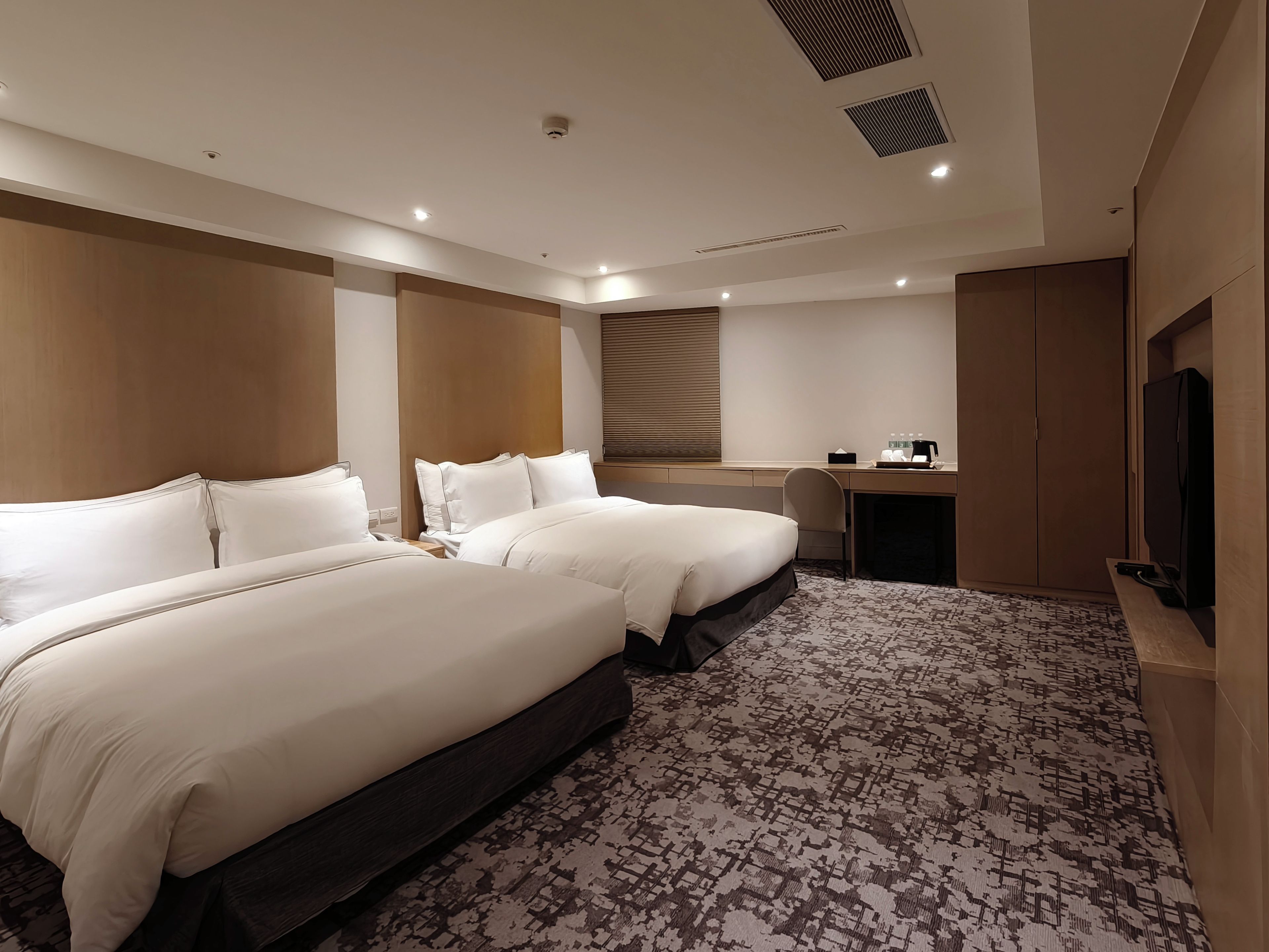 A hotel room with two beds, a desk, a television, and a wardrobe.