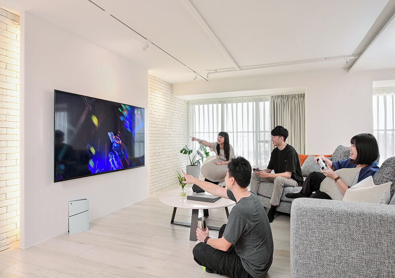 A modern living room with a large flat-screen TV, a round coffee table, and a brick wall.