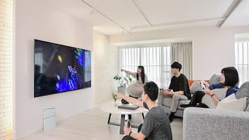 A modern living room with a large flat-screen TV, a round coffee table, and a brick wall.