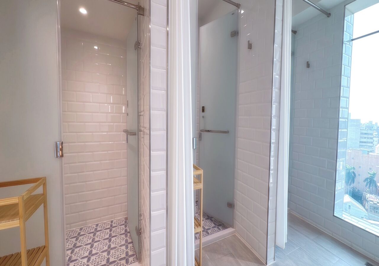 A modern bathroom with a glass shower enclosure, white tiled walls, and a patterned floor.