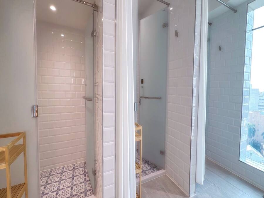 A modern bathroom with a glass shower enclosure, white tiled walls, and a patterned floor.