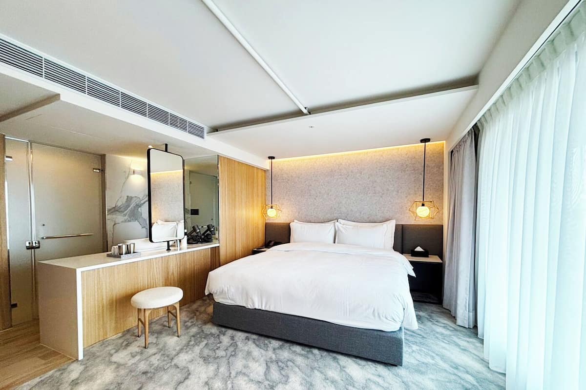 A modern hotel room with a large bed, a vanity with a mirror, and a desk.
