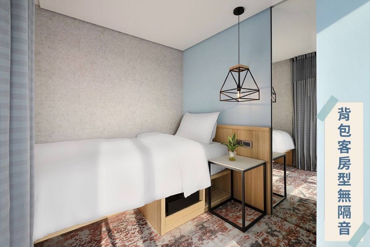 A hotel room with a bed, bedside table, and a mirror.