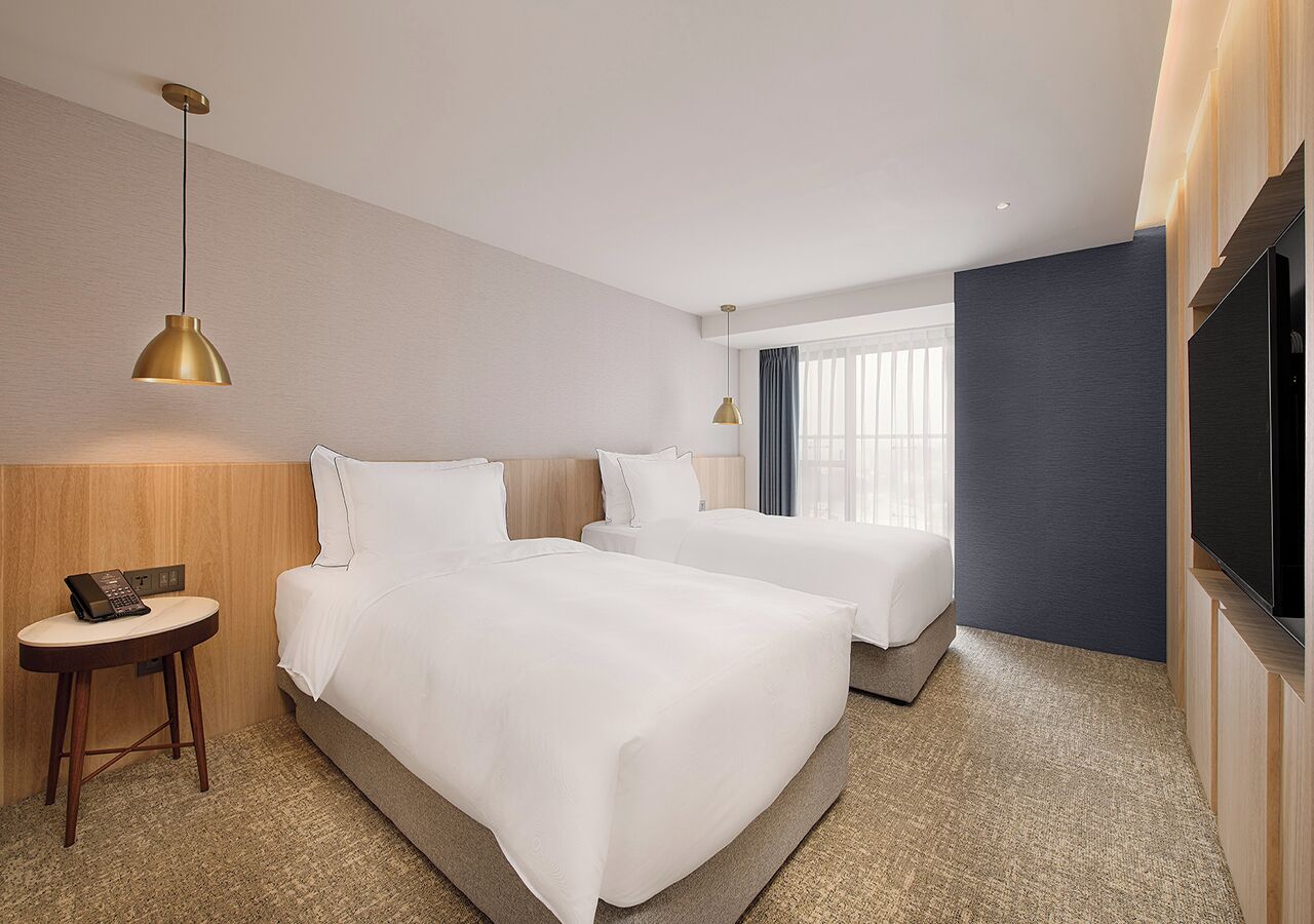 Habitación de hotel con dos camas, una mesita con un teléfono y un televisor en la pared.