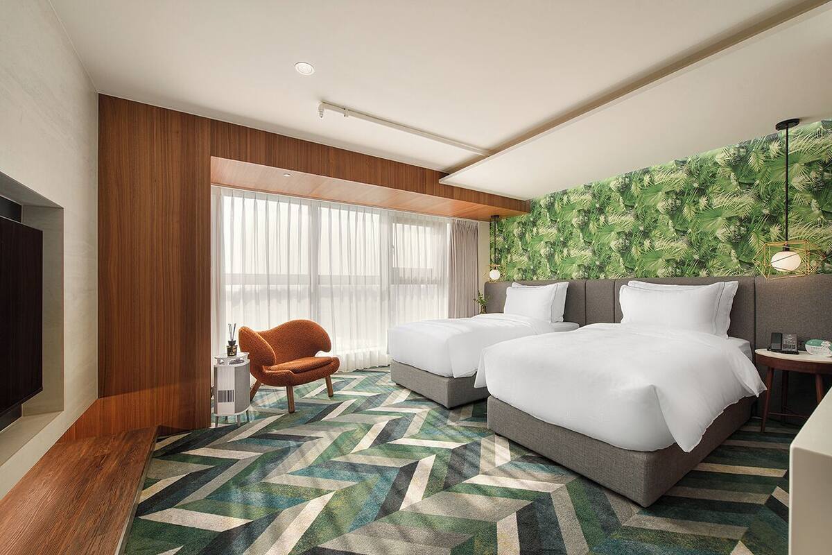 A hotel room with two beds, a TV, a chair, a desk, and a large window with curtains.
